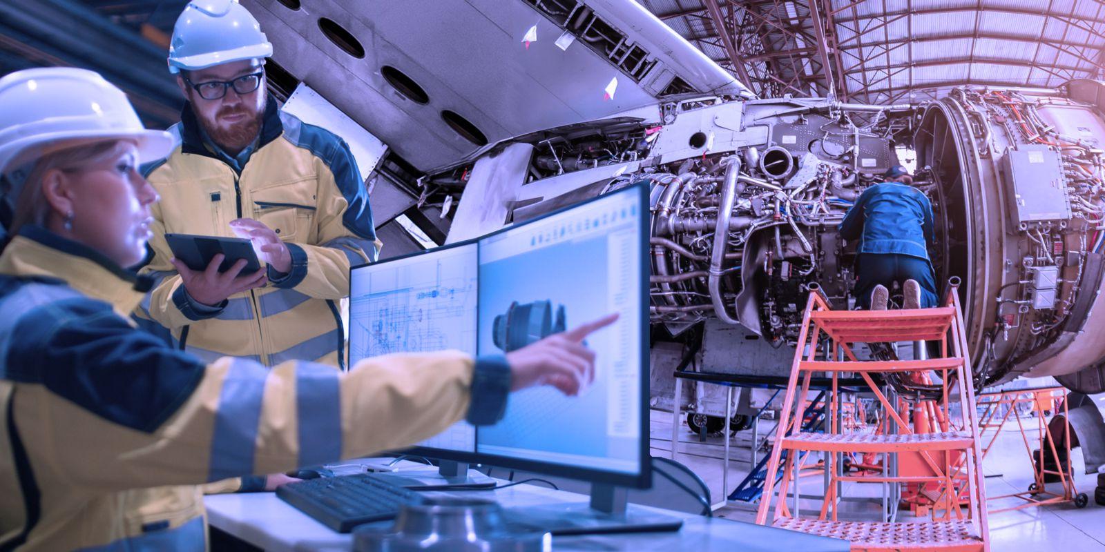 一个机械师跪在一个橙色的安全梯上修理飞机引擎. 一男一女工程师身穿黄黑夹克，头戴安全帽，在电脑显示器和平板电脑前研究计划.